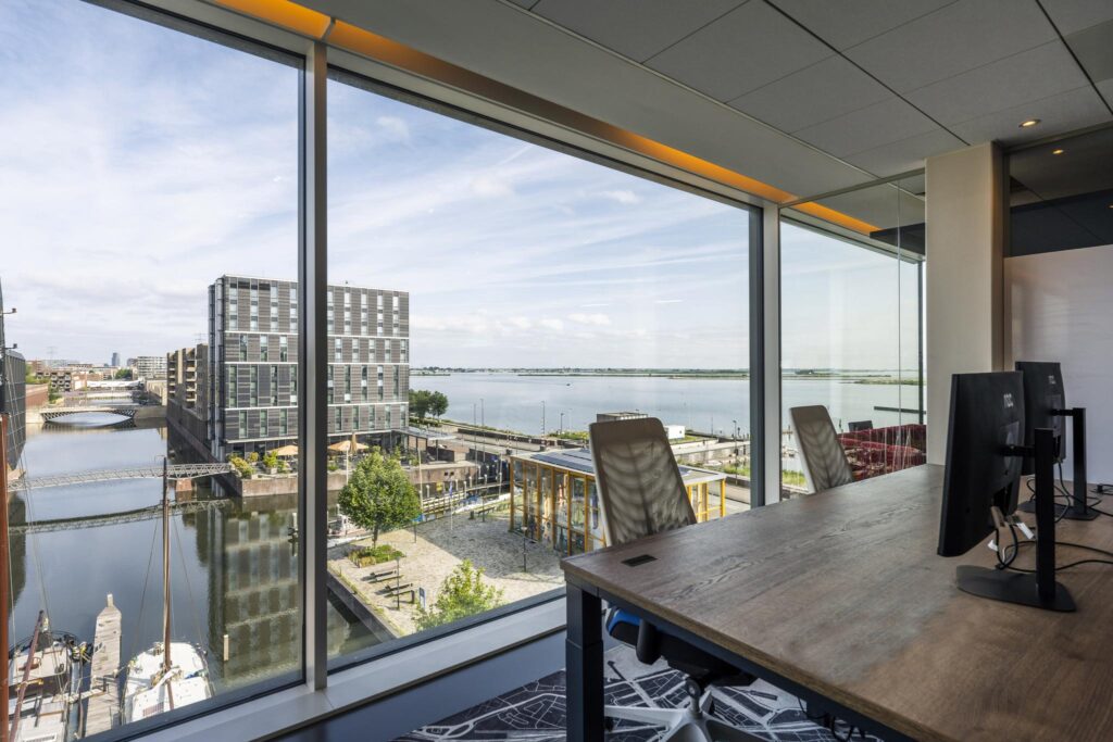 Modern office space with large windows offering a view of Krijn Taconiskade and the waterfront in Amsterdam.